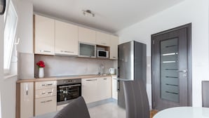 A modern kitchen with beige cabinets, a microwave, a refrigerator, and an oven. There is a dining table with chairs and a vase with flowers on the counter. - Urban Villa Penthouse (Podstrana)