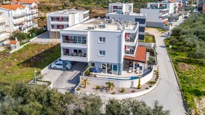 A modern multi-story building with a curved driveway, a covered outdoor seating area, and a parking lot. - Urban Villa Penthouse (Podstrana)