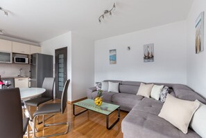 A modern living room with a grey sofa, a dining table with chairs, and a kitchen area with a microwave and cabinets.