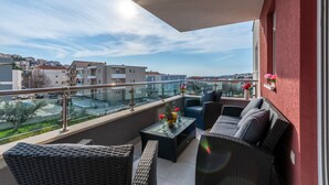 A balcony with wicker furniture, a glass table, and a view of a residential area. - Urban Villa Penthouse (Podstrana)