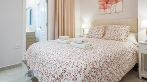 Une chambre à coucher bien aménagée, avec un lit, deux tables de chevet, une œuvre d’art accrochée au mur et une porte donnant sur une salle de bain.