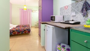 A compact room with a bed, a small kitchenette, a microwave, and a trash bin. - Ni-Mar Studios & Apartments (Zakynthos)
