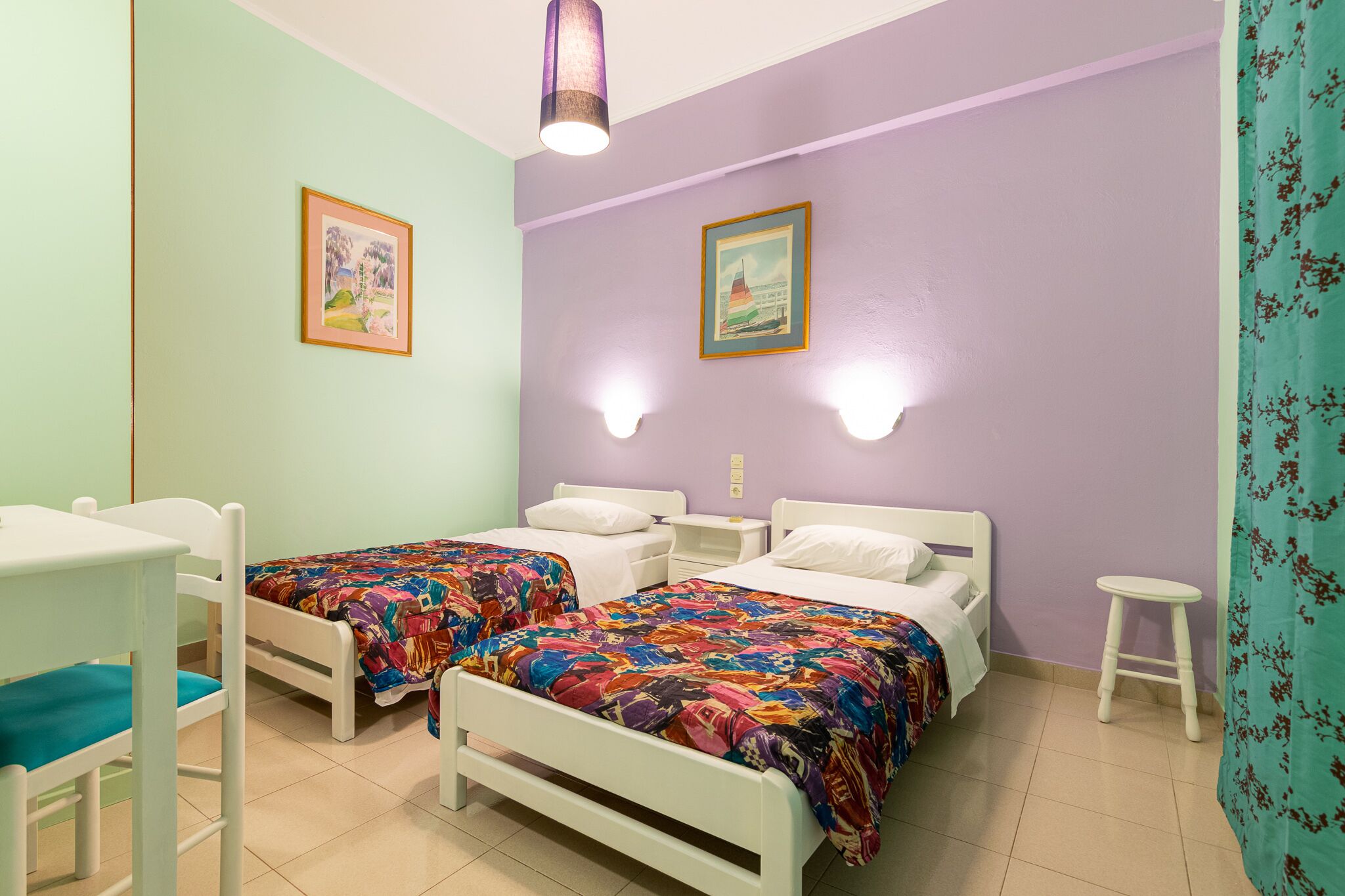 Habitación con dos camas, un escritorio y una silla. Hay dos luces fijadas a la pared y dos cuadros enmarcados.