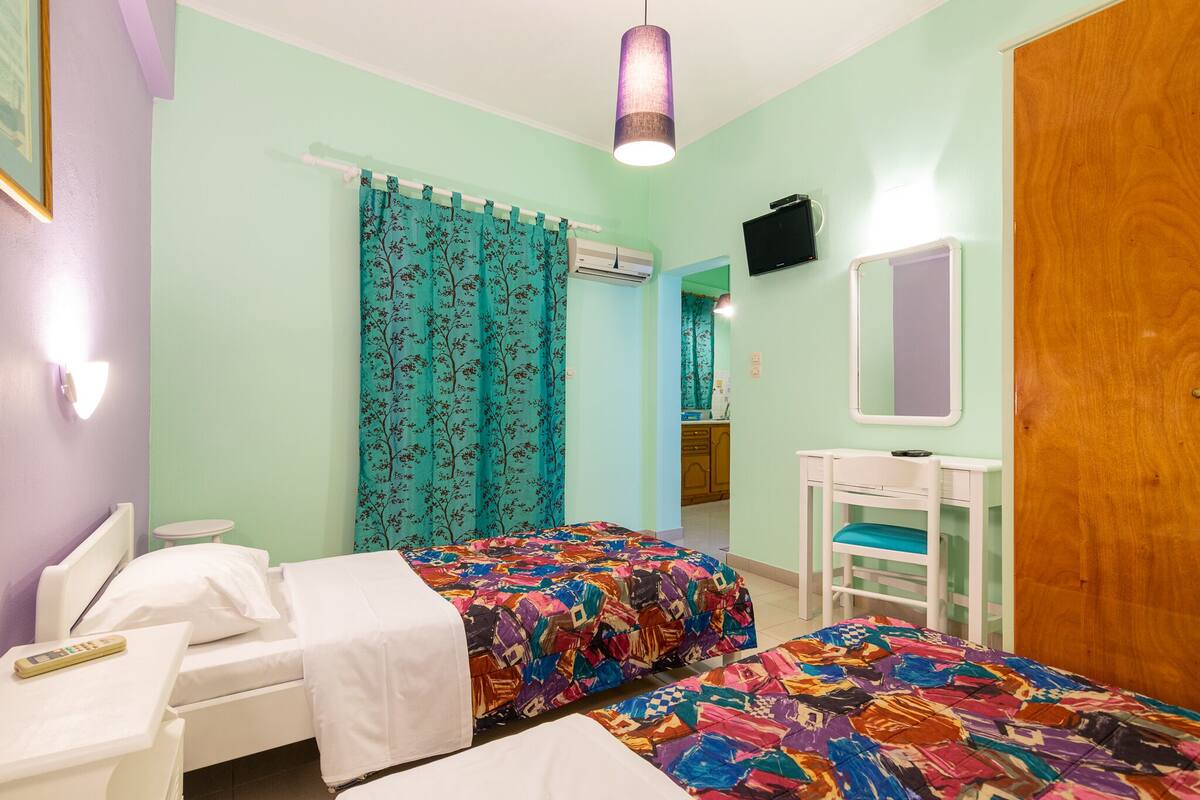 Ein Schlafzimmer mit zwei Betten, einem Schreibtisch, einem Stuhl, einem Spiegel und einem Fernseher.