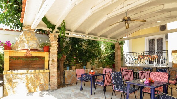 An outdoor patio with stone flooring, a brick fireplace, and red and white patterned chairs. - Ni-Mar Studios & Apartments (Zakynthos)