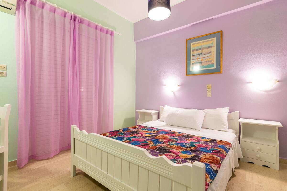 Ein Schlafzimmer mit einem Bett, zwei Nachttischen, einem Fenster mit Vorhängen und einer Wandleuchte.
