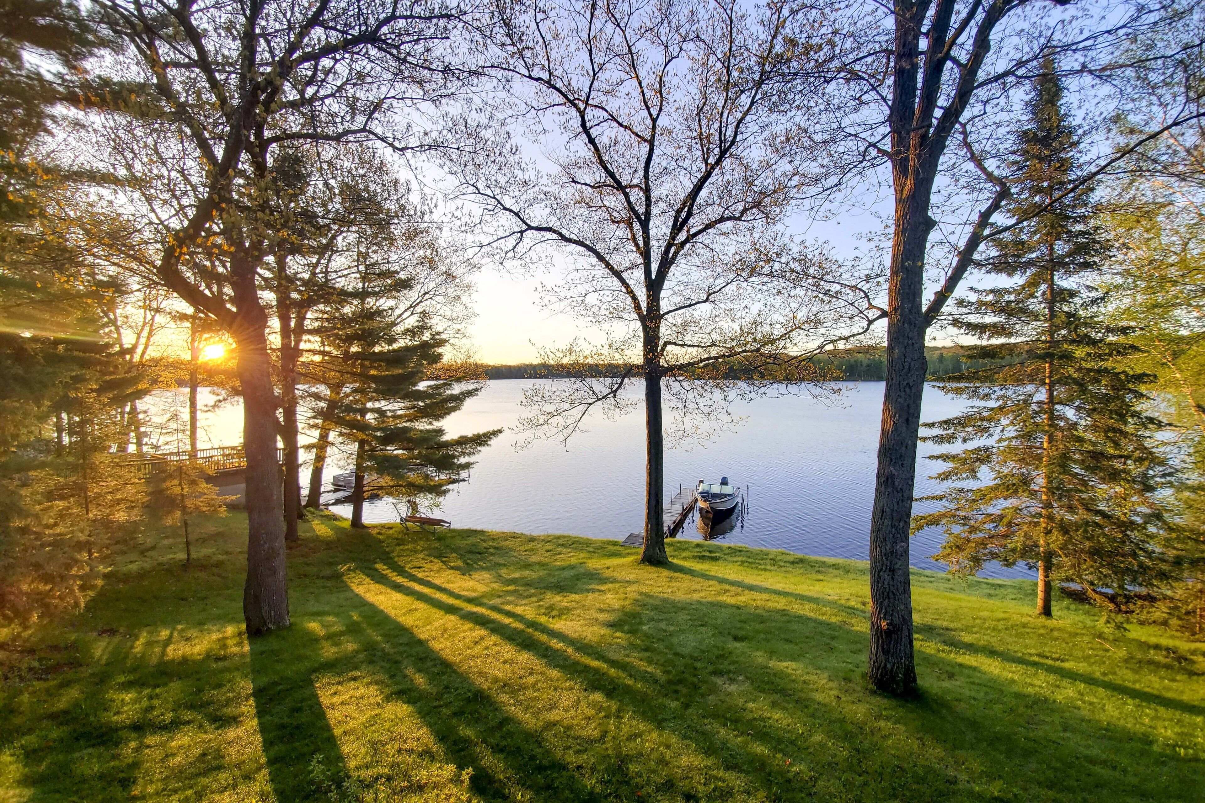 Una vista tranquilla su un lago con un molo e una barca, immersa tra alberi ed erba.
