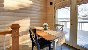 Interior de madera con una mesa, sillas y vistas a un paisaje nevado a través de un ventanal.