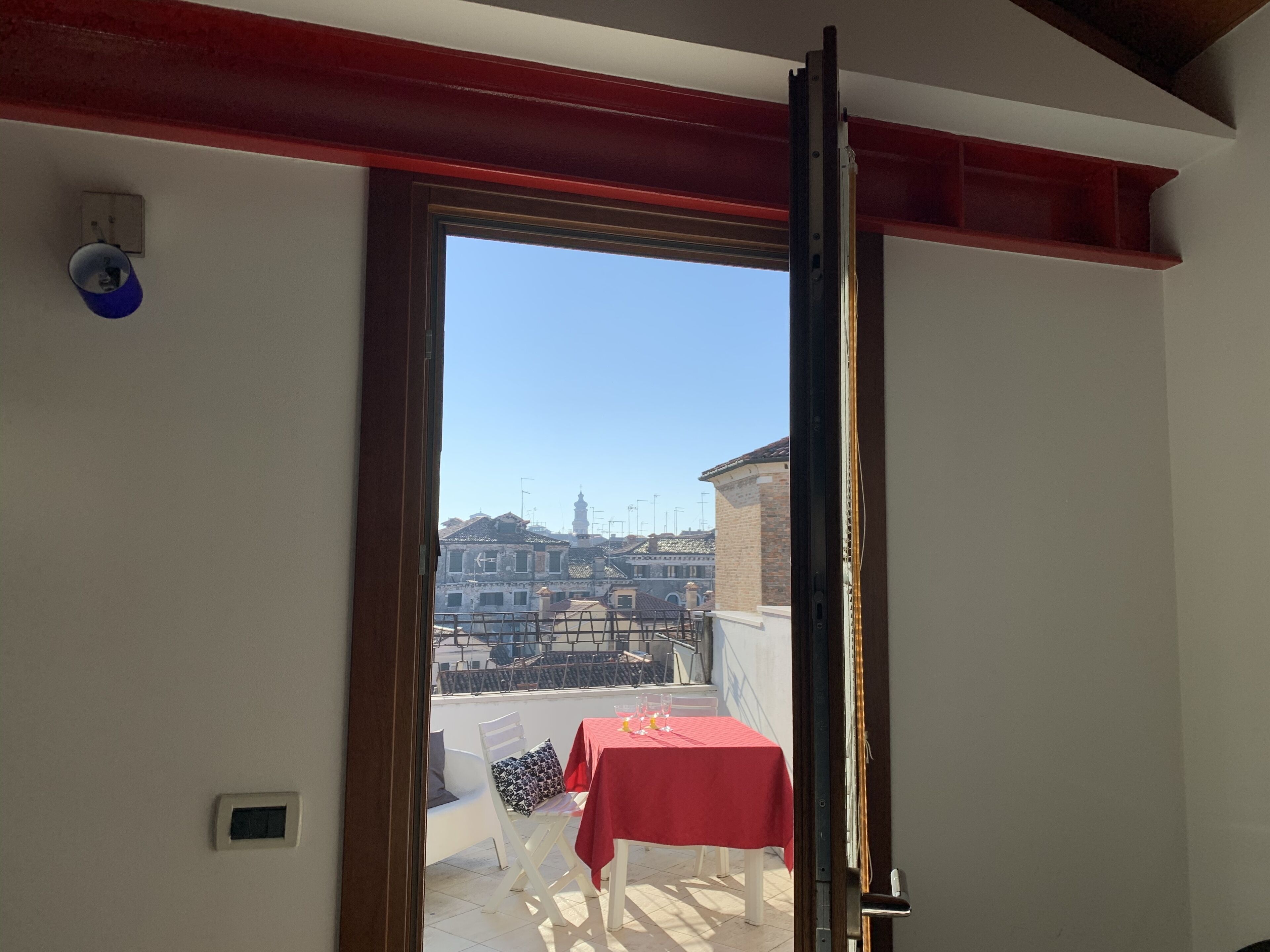 Une pièce avec un balcon, une table rouge et une chaise.