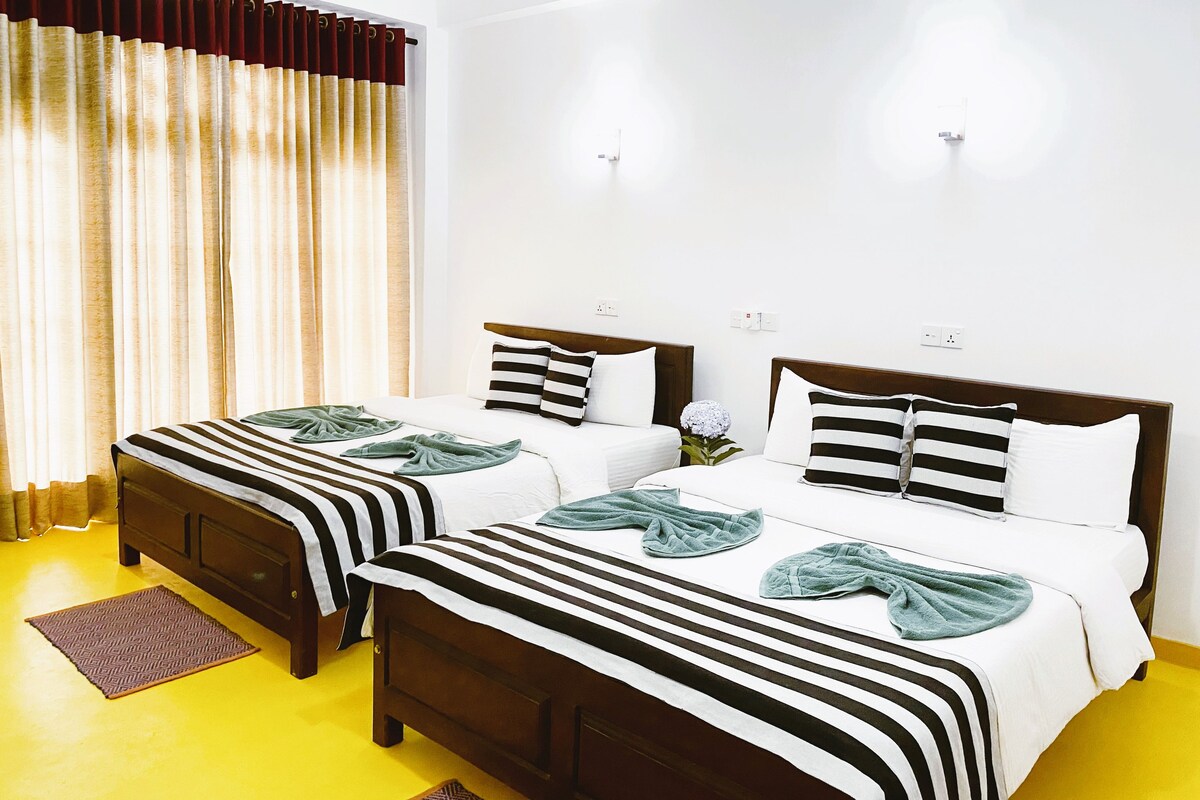 A hotel room with two beds, a yellow floor, and a window with curtains.