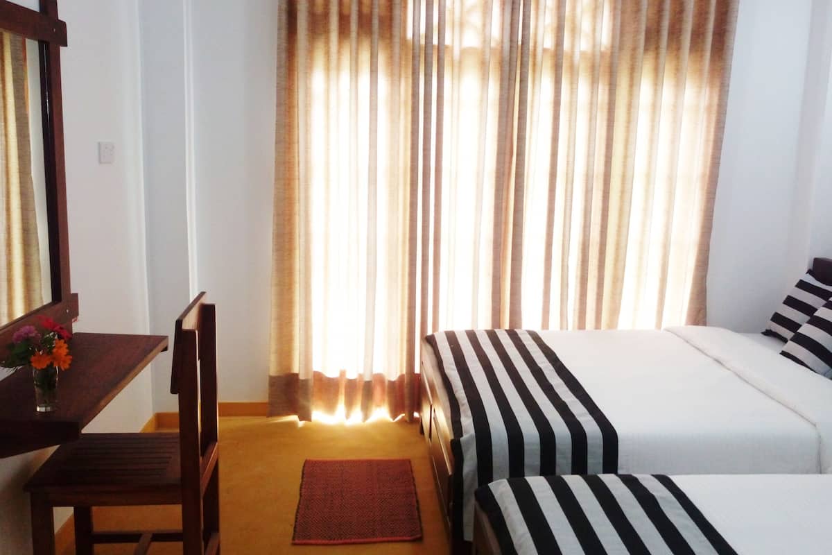 Habitación de hotel con cama, una silla, una mesita con un florero y una ventana con cortinas.