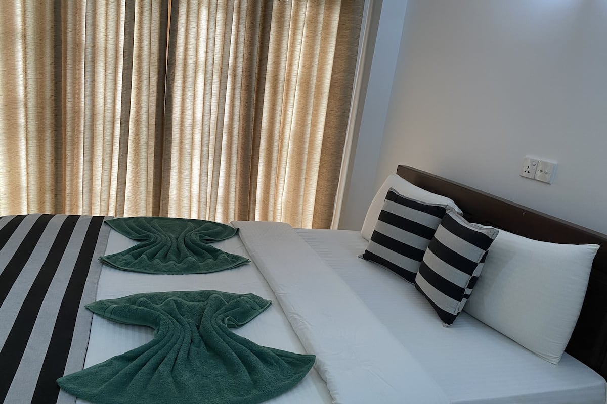 Una cama bien hecha con almohadas a rayas y lisas, una toalla verde y un edredón a rayas.