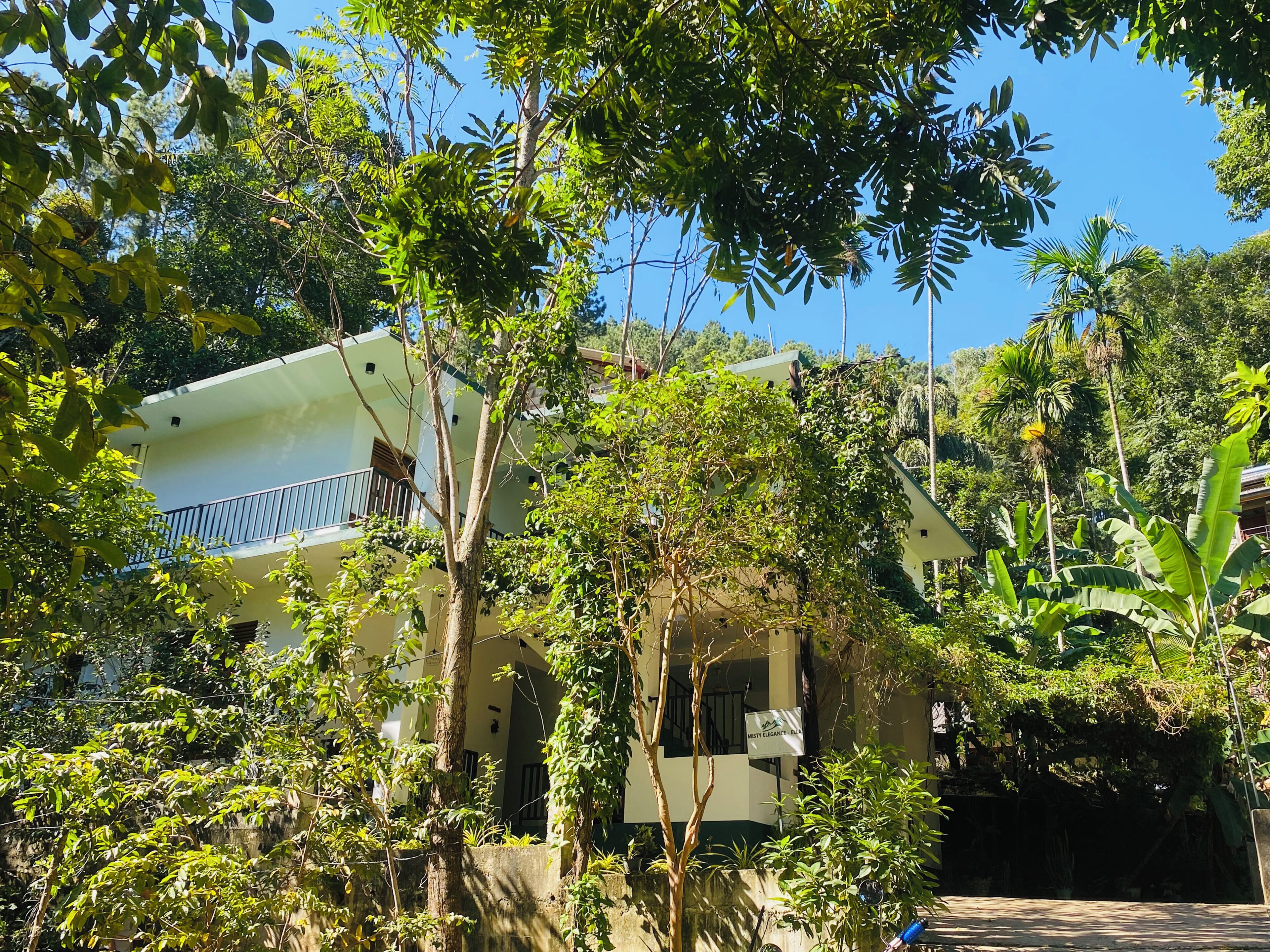 Um edifício com varanda, rodeado por vegetação densa e árvores.