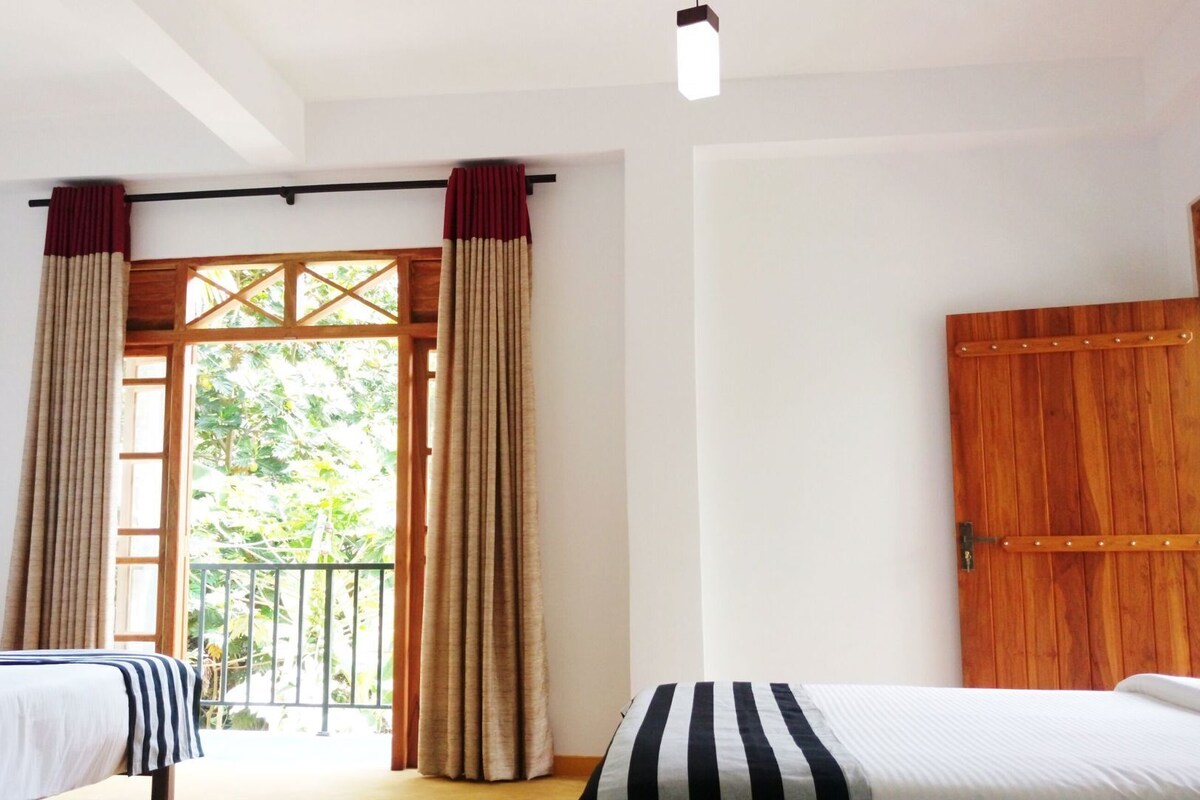 A room with two beds, a wooden door, and a balcony with curtains.