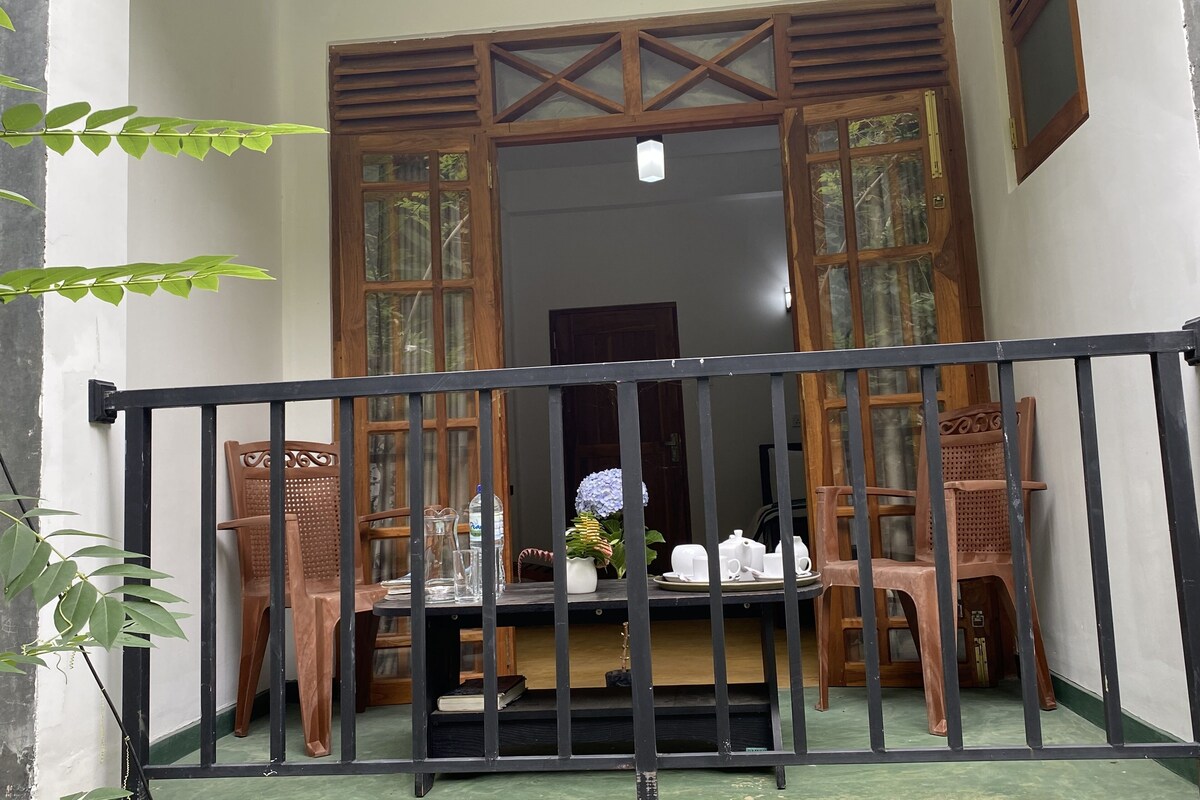 Un balcon avec une table dressée pour le thé, entouré de chaises en bois et muni d’une balustrade.