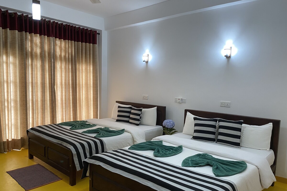 A hotel room with two beds, a large window with curtains, and wall-mounted lights.