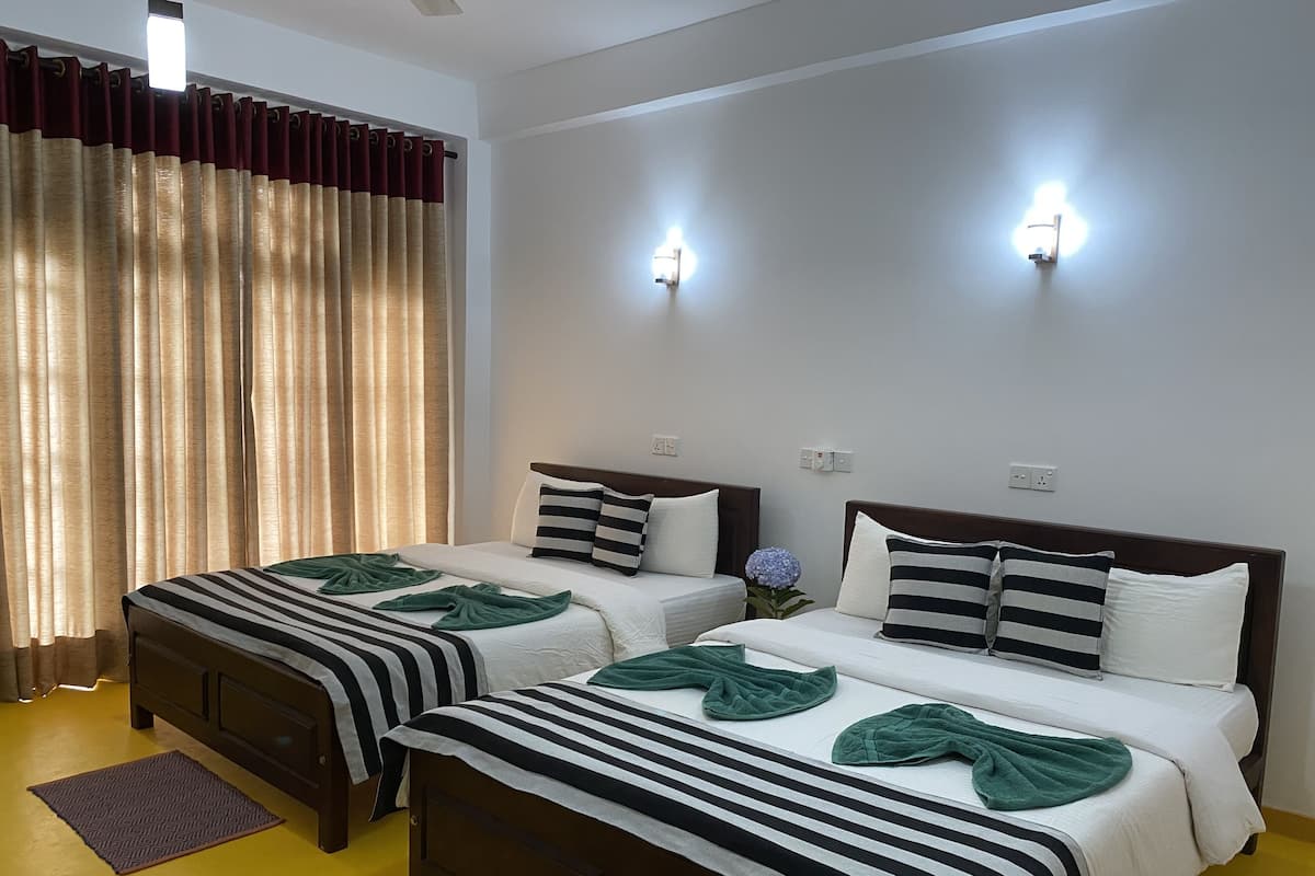 Habitación de hotel con dos camas, un ventanal grande con cortinas, luces fijadas a la pared y suelo amarillo.