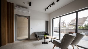 A modern waiting area with a sofa, two armchairs, a small table, and a large window offering a view of the outside. - Marina Apartments (Wroclaw)