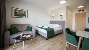 A modern hotel room with a bed, sofa, and a small dining table. - Marina Apartments (Wroclaw)