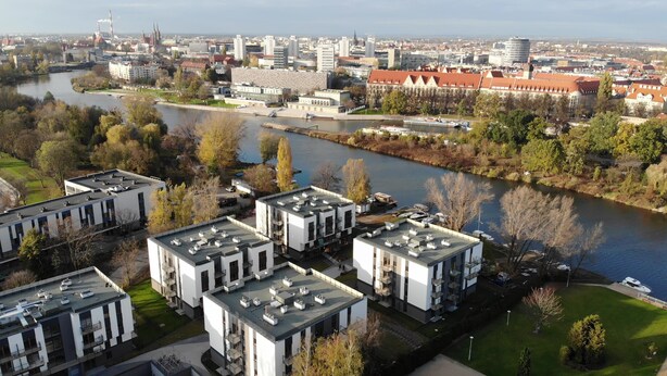 A modern building complex with multiple apartment buildings, a river, and a cityscape in the background. - Marina Apartments (Wroclaw)