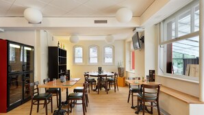 Un comedor amplio con mesas y sillas de madera, ventanas grandes con vidrieras decorativas y un diseño moderno de techo.