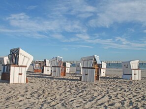 Strandhütten mit Nummern, auf einem Sandstrand aufgereiht, im Hintergrund ein Steg.