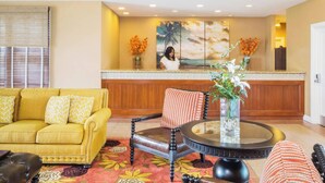 A lobby with a yellow sofa, a round table with a vase, and a reception desk with a painting. - Hyatt Windward Pointe 2 Bedroom (Key West)