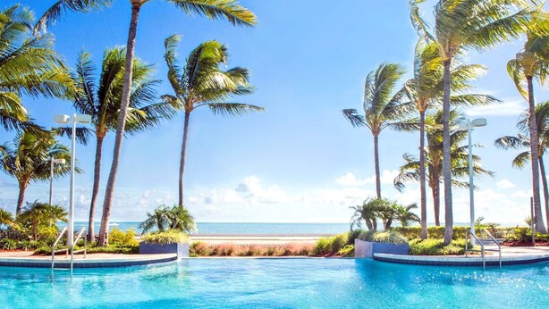 A pool area with clear blue water, surrounded by palm trees and a view of the ocean. - Hyatt Windward Pointe 2 Bedroom (Key West)