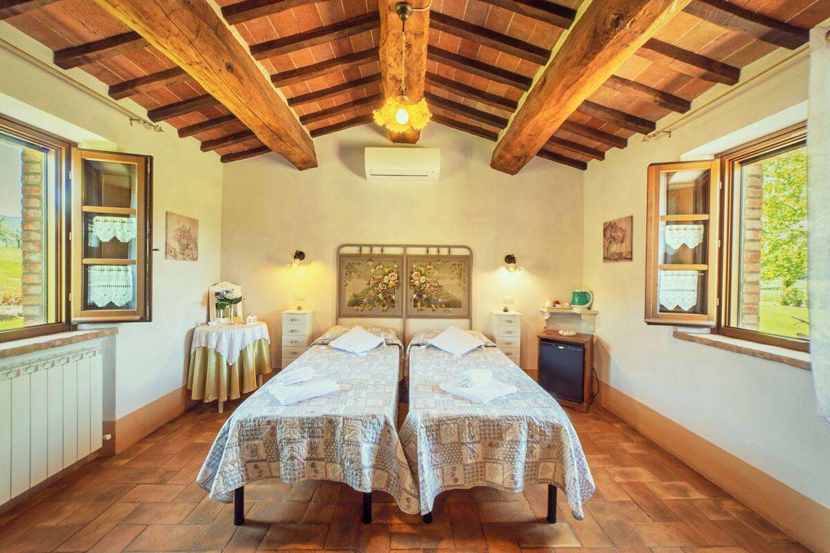 Una habitación con dos camas, vigas de madera en el techo, aire acondicionado y una ventana con vista a la vegetación.