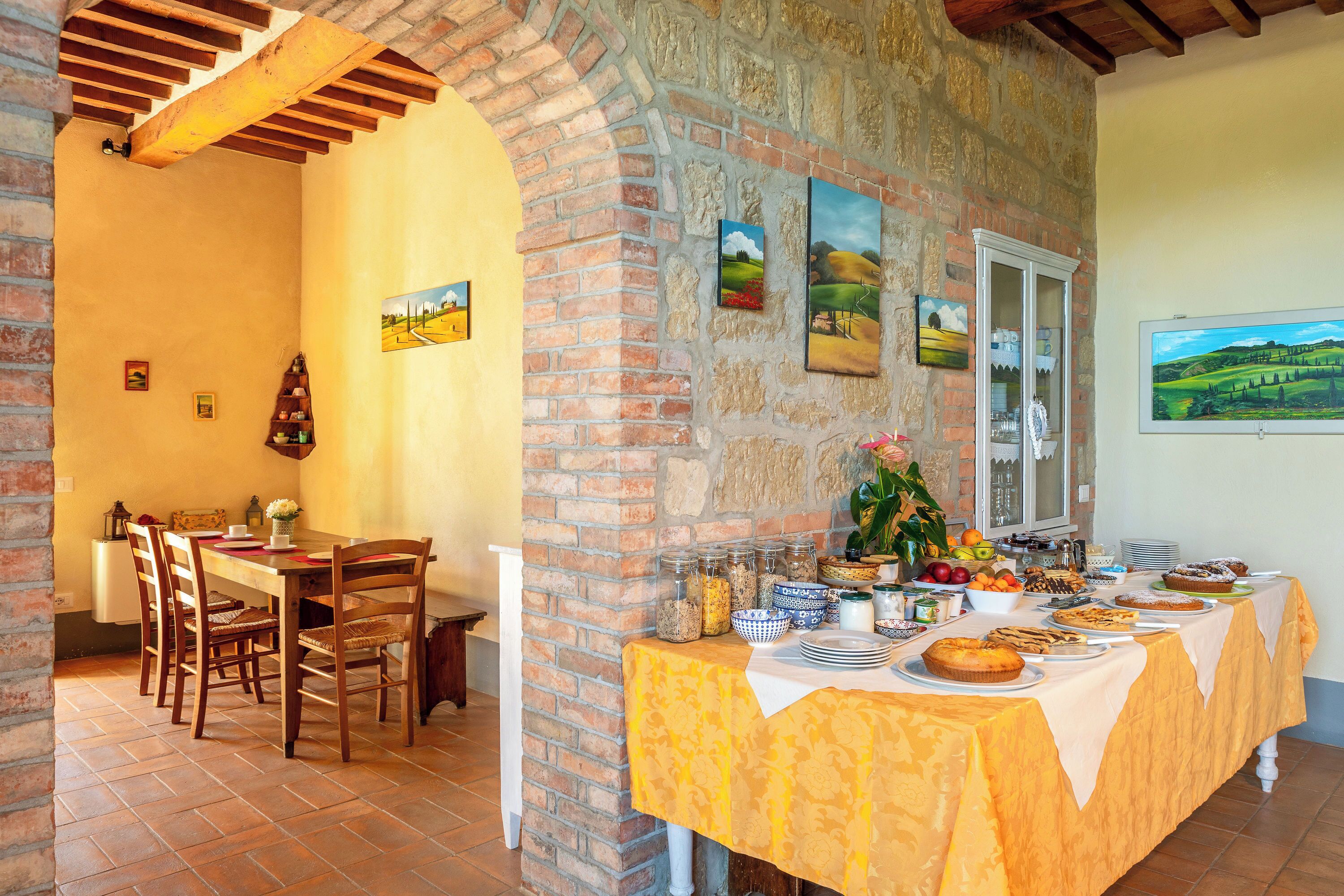 Un'area pranzo con parete in mattoni, sedie di legno, un tavolo con tovaglia gialla e diversi piatti.