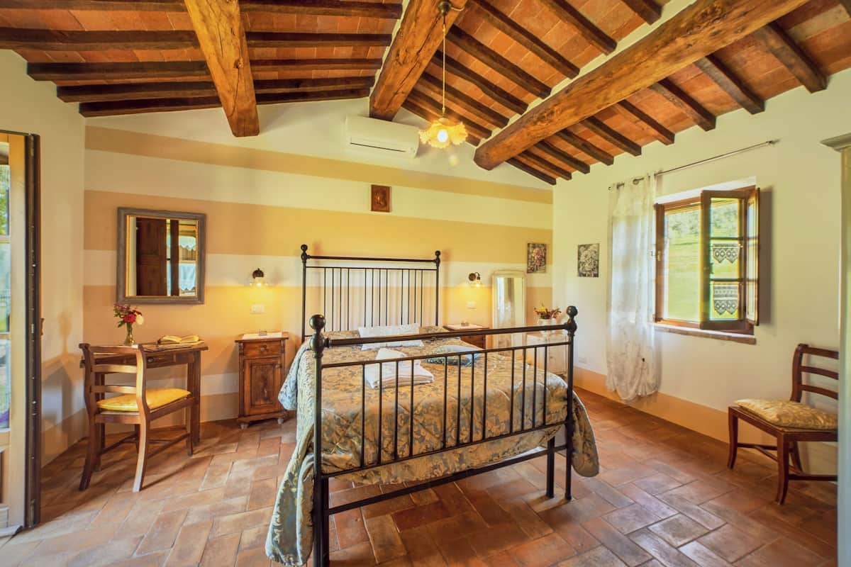 Un dormitorio con una cama de madera, una silla de madera, una mesita y una ventana con cortinas.