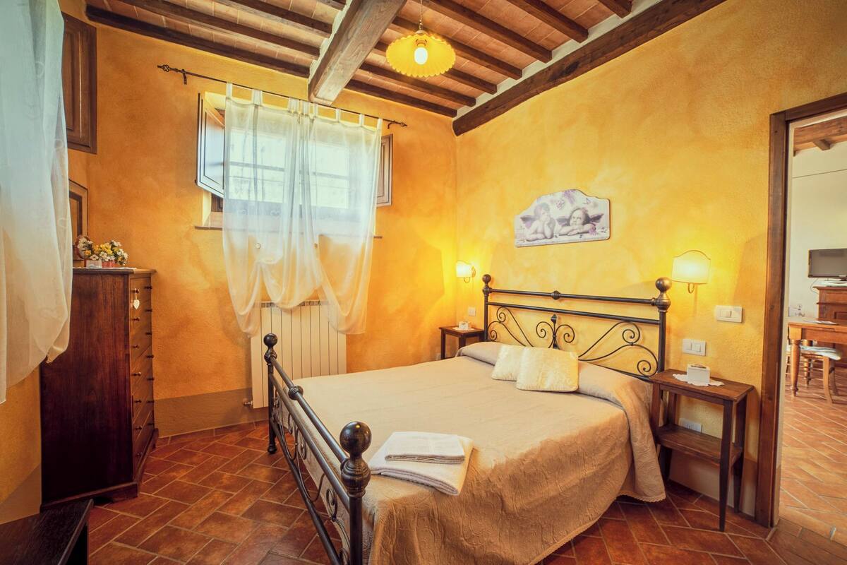 Un dormitorio con cama, mesita de noche, cómoda, ventana con cortinas y un cuadro en la pared.