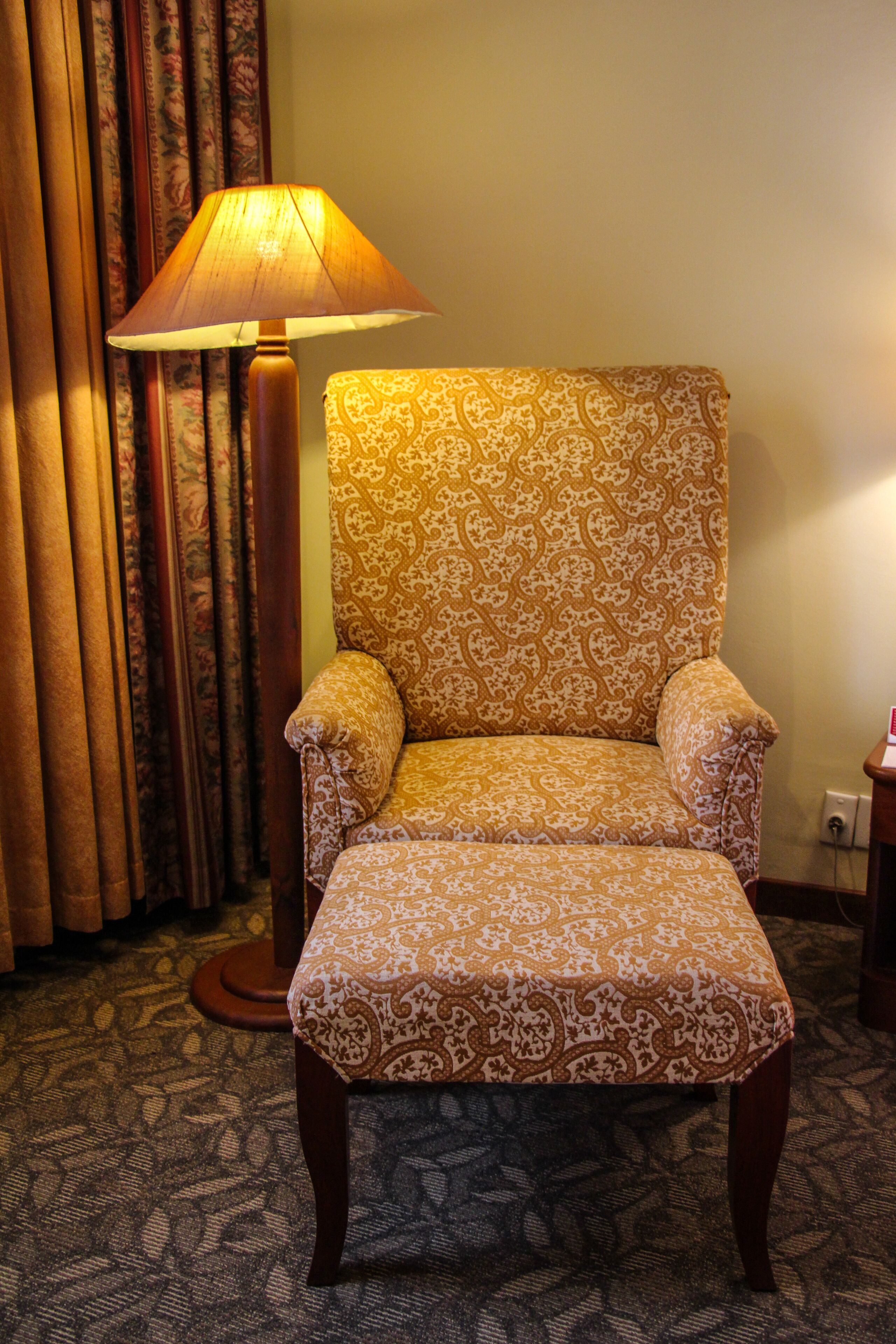A chair with a patterned fabric, a floor lamp, and curtains in a room.