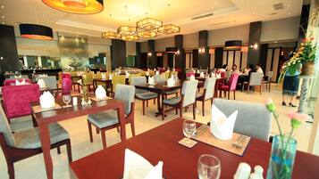 A hotel dining area with multiple tables and chairs, a bar in the background, and a modern chandelier.
