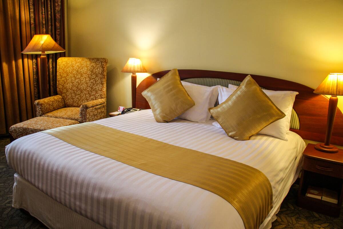 A hotel room with a large bed, two bedside lamps, a chair, and a nightstand.