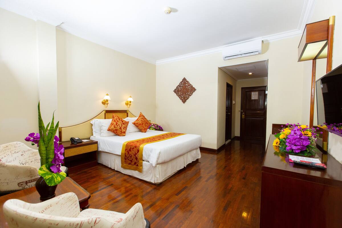 A hotel room with a bed, bedside tables, a desk, a chair, and a wall-mounted TV.