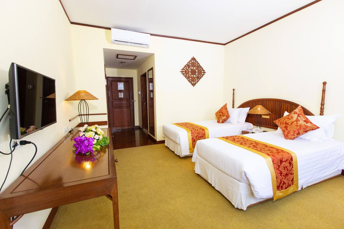 A hotel room with two beds, a TV, a desk, and a lamp.