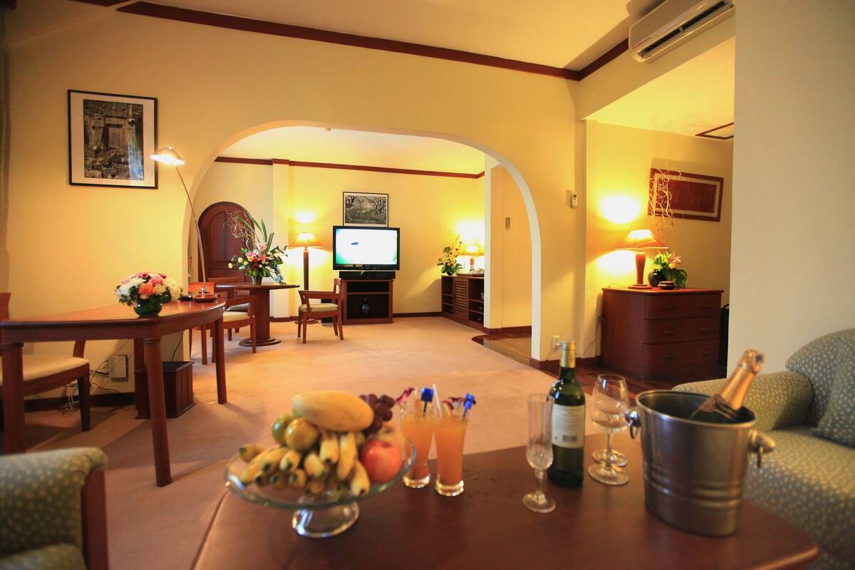 A cozy living room with a dining area, a television, and a dining table set with fruits and drinks.