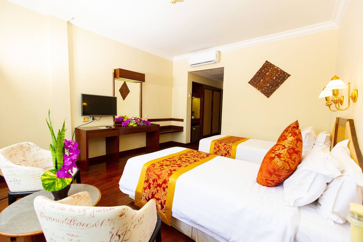 A hotel room with two beds, a desk, a chair, and a television.