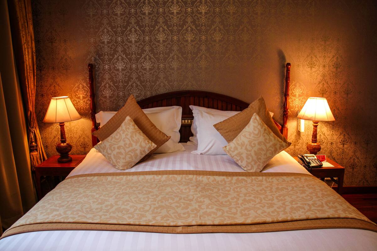 A neatly made bed with a patterned bedspread and pillows, two bedside lamps, and a telephone on the nightstand.