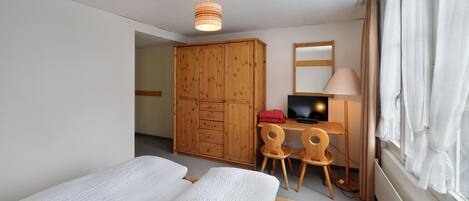 A hotel room with a bed, a desk with a computer, a wardrobe, and a window with curtains.