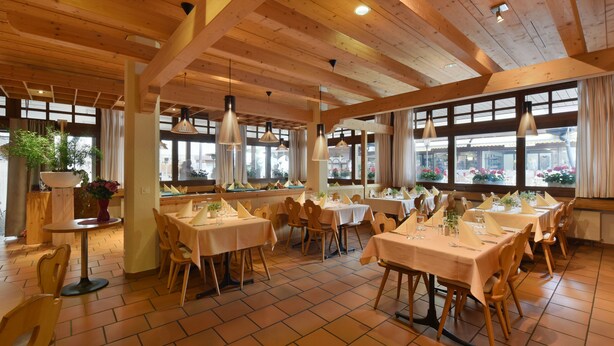 Un restaurant avec des poutres en bois, de grandes fenêtres et des tables dressées pour le service.