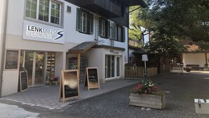 Un bâtiment avec une enseigne indiquant « LENKMILCH SPECIALITÄTEN » et une autre indiquant « Kidsclub ». On y trouve des tableaux noirs avec des plats au menu et un jardinier en bois rempli de fleurs.