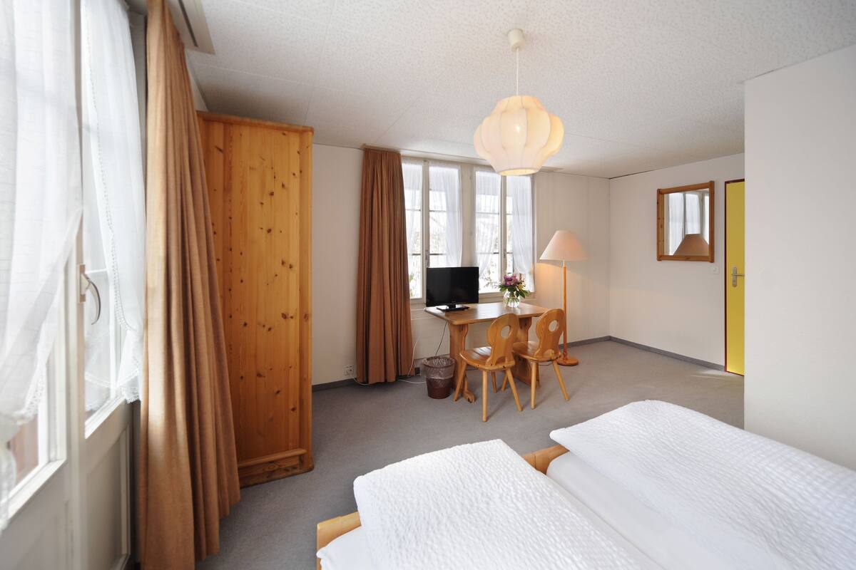 A hotel room with two beds, a desk with a computer, a chair, a lamp, and a television.