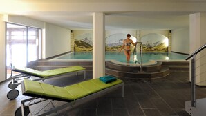 Un espace de bien-être comprenant une piscine, des chaises longues et une fresque représentant des montagnes.