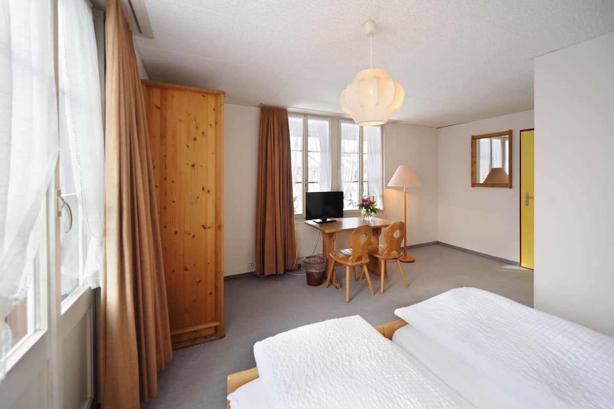 A hotel room with two beds, a desk with a computer, a chair, a lamp, and a TV.