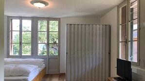 Une chambre à coucher avec un lit, un téléviseur posé sur une commode en bois et une fenêtre avec des rideaux.