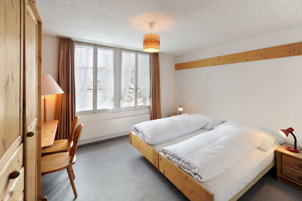 A room with a bed, a desk, a chair, a lamp, and a window with curtains.