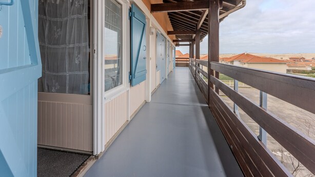 A covered balcony with a wooden railing, a view of the surrounding buildings, and a clear sky. - Spacious Duplex for 6, 300m from Ocean, 2 Bedrooms, South Balcony (Biscarrosse Plage)