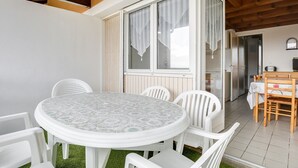 A dining area with a round table and white chairs, a window with curtains, and a kitchen visible through an open door. - Spacious Duplex for 6, 300m from Ocean, 2 Bedrooms, South Balcony (Biscarrosse Plage)